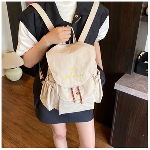 Detail view of beige canvas backpack featuring 'take it easy' embroidery and side drawstrings