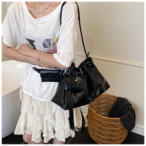Détail macro du sac seau en cuir verni noir brillant avec sa mini pochette assortie et cordon