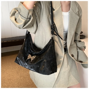 Detail of glossy black pleated tote bag featuring a silver metal butterfly buckle accent