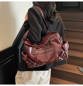 Close-up of a burgundy leather tote with multiple zippers and metallic buckles on the strap