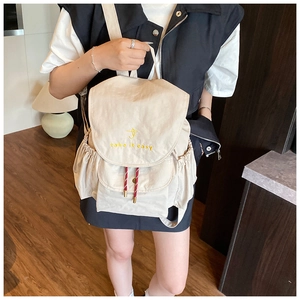 Detalle de mochila de lona beige con bordado 'take it easy' y cierre de cordón