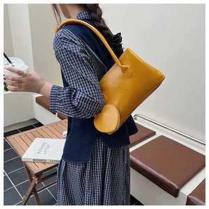 Dettaglio della borsa sottobraccio giallo brillante con ciondolo rotondo e ecopelle lucida