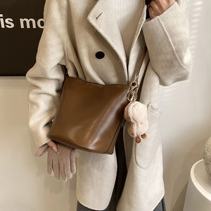 Brown leather bucket bag with plush charm shown on model in minimalist warm-toned setting