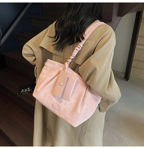 Sac bandoulière rose en similicuir plissé avec bandoulière décorative porté par femme