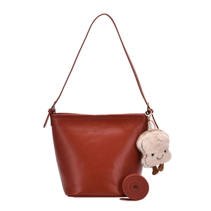 Minimalist caramel brown leather bucket bag with a cute plush toast charm and slim shoulder strap