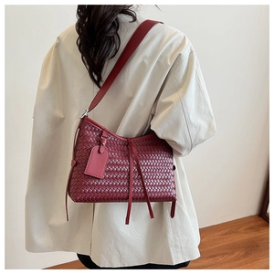 Detail of burgundy woven crossbody bag featuring leather texture and decorative tassels