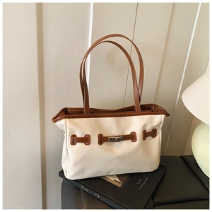 Detail of a canvas tote with dark brown leather straps and silver twist-lock closure