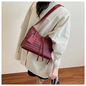 Detail of wine red woven leather shoulder bag with tassels shown on a model