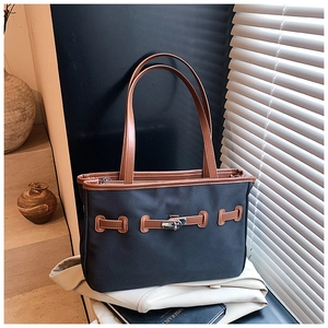 Detail of color-block tote bag featuring leather handles and silver twist lock closure