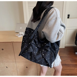 Side view of a large black canvas tote bag with star prints and a bow on a model