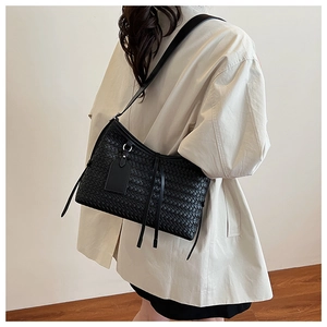 Side view of black woven shoulder bag with side fringes and minimalist strap detail