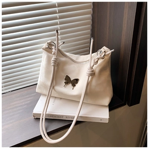 Detail of cream velvet tote bag featuring metal butterfly ornament and knotted shoulder strap