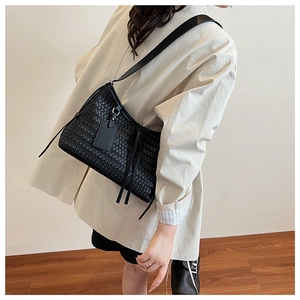 Detail shot of black woven shoulder bag with chic side tassels and long leather strap