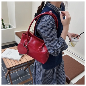 Dettaglio borsa sottobraccio rossa lucida con ciondolo a cuore su outfit blu a contrasto