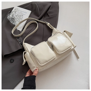 Detailed view of cream patent leather crossbody bag with multiple zipper pockets on a blazer
