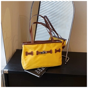 Detail of a contrast color yellow tote bag with silver twist lock and brown leather strap