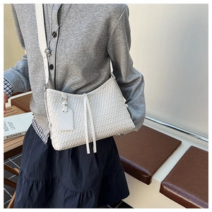 Detail of white woven bucket bag featuring elegant long tassels and adjustable shoulder strap