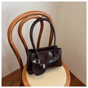 Dettaglio di una borsa in pelle lucida marrone scuro con ciondolo a cuore su sedia di legno