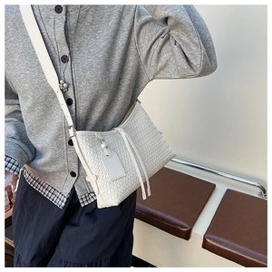 Detail of white woven crossbody bucket bag showing the texture and tassel detail