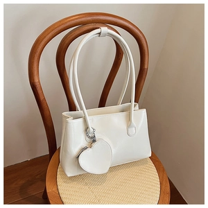 Dettaglio di una borsa a spalla bianca minimalista con pochette a cuore su sedia