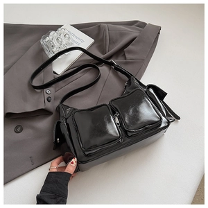 Close-up of black patent leather shoulder bag with multiple functional zipper pockets