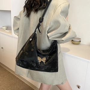 Chic black hobo bag with golden butterfly detail and knot strap shown on shoulder