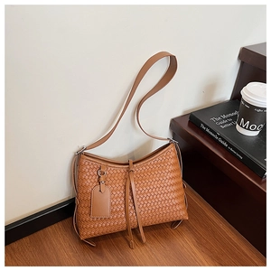 Detail of tan woven texture shoulder bag with stylish tassels on a wooden step