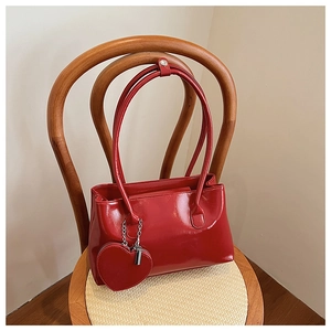 Borsa a mano in vernice rossa con ciondolo a cuore coordinato su sedia vintage