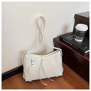 Close-up of white woven bucket bag with leather strap next to lifestyle props