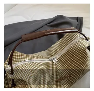 Close-up of green checkered tote bag showing silver double zippers and brown handles