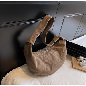 Detail of a large brown canvas croissant bag with pleated texture on a white bed