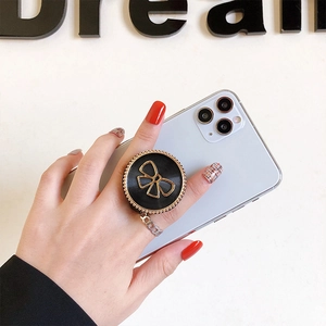 Black phone grip with golden bow and chain decoration on a smartphone back