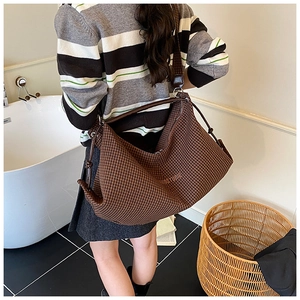 Close-up of a brown checkered canvas tote bag with JOSTUDIO logo worn on a shoulder