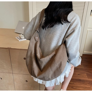 Detailed view of the large brown crescent canvas shoulder bag worn by a model