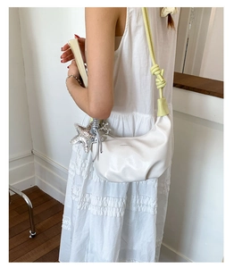 Detail of white crescent bag with lime green knotted strap and silver star pendant
