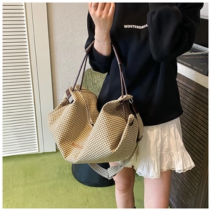Detail of a large brown gingham tote bag with leather handles and woven shoulder strap
