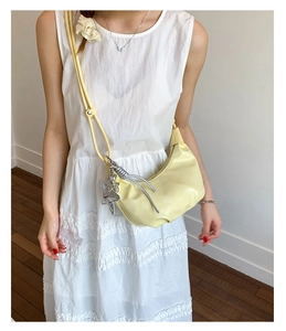 Detail of pale yellow crescent leather bag with silver star charm on white dress