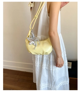 Detail of pale yellow half-moon bag with metallic star charm on white dress outfit