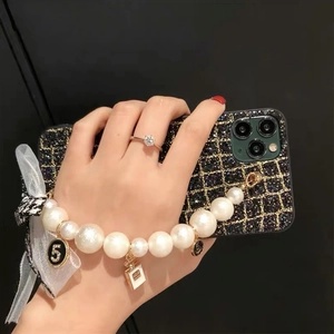 Detail of iPhone case with black gold plaid, large pearl wrist chain and bow charm