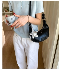 Detail of black crescent shoulder bag with star charm worn by a model in casual setting