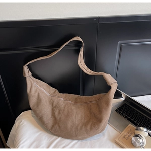 Close-up of brown suede croissant bag featuring segmented stitching and metal zipper detail