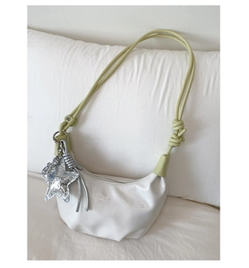 Close-up of a white crescent bag with green knotted strap and silver star charm detail