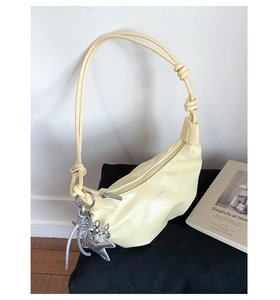 Detail of cream croissant bag with silver star charm and knotted strap on minimalist decor