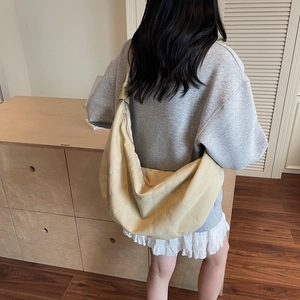 Large beige canvas hobo bag with vertical stitching shown on model in minimalist interior