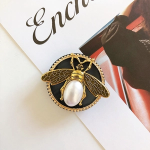 Detailaufnahme einer Vintage-Bienen-Handyhalterung mit großer Perle und goldenem Rahmen