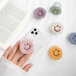 Plush smiley face phone grip set in pastel colors on minimalist fabric background