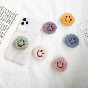 Plush smiley face folding air cushion phone grips in assorted colors on a white background