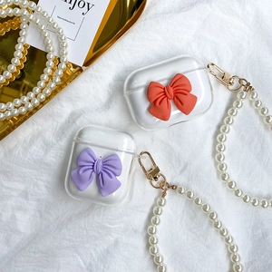 Detail of clear AirPods case with 3D bow decoration and pearl handle chain on white fabric