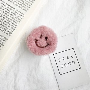 Close-up of pink plush phone grip with a cute embroidered smiley face on fabric