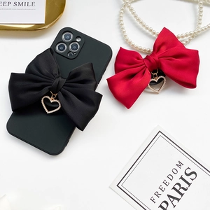 Detail view of large satin bow phone grip with pearl heart pendant in black and red